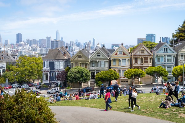 San Francisco's famous "Painted Ladies" Victorian homes are shown in the background with people relaxing and socializing at the park in the foreground